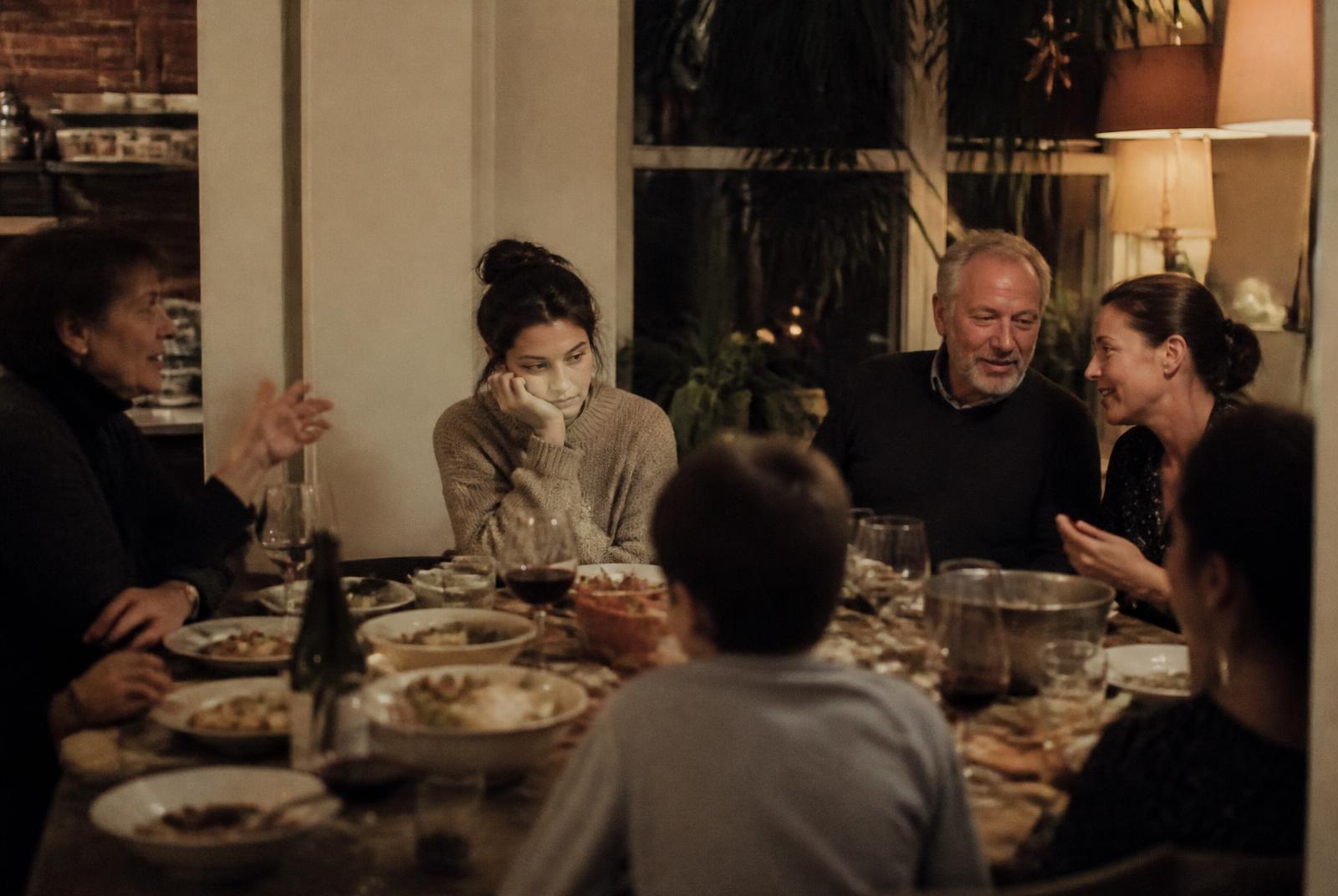 Extended family gathered around a dinner table while one woman sits quietly, illustrating the challenge of setting boundaries with family