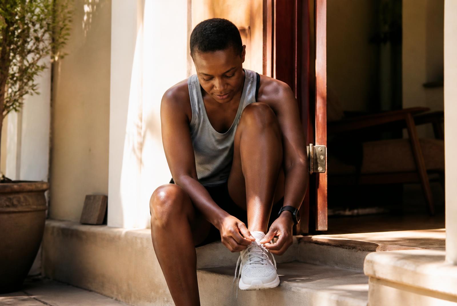 Person in their thirties calmly lacing up running shoes by a sunlit doorway early in the morning, beginning a healthy habit